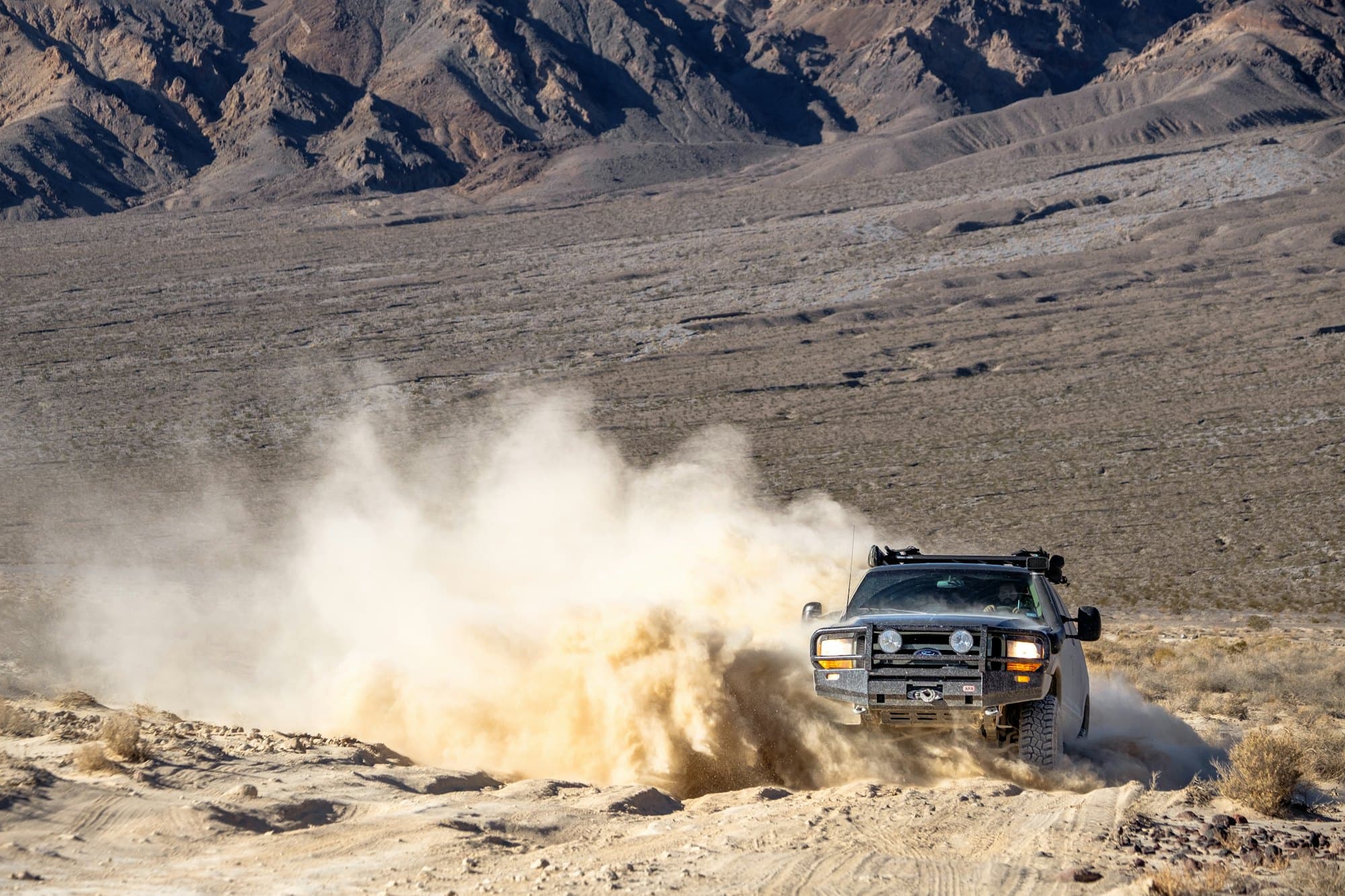 A rugged 4x4 powering through the desert, kicking up a cloud of sand
